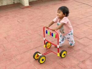 fille en robe à fleurs blanche et rose conduisant un tricycle rouge et jaune