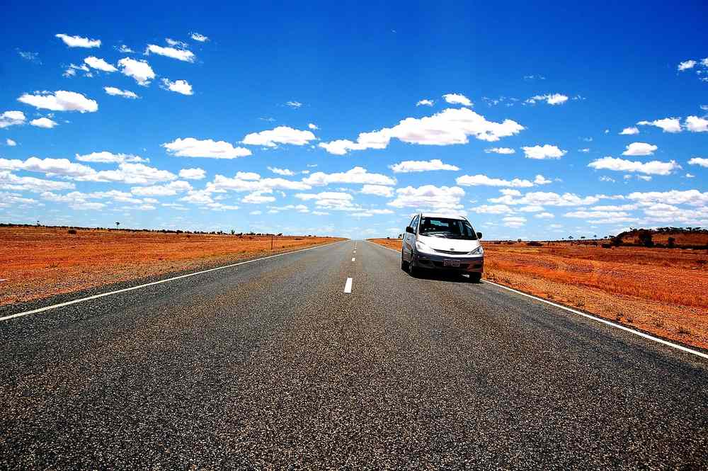 Une voiture blanche circulant seule sur une route asphaltée, paysage désertique alentour