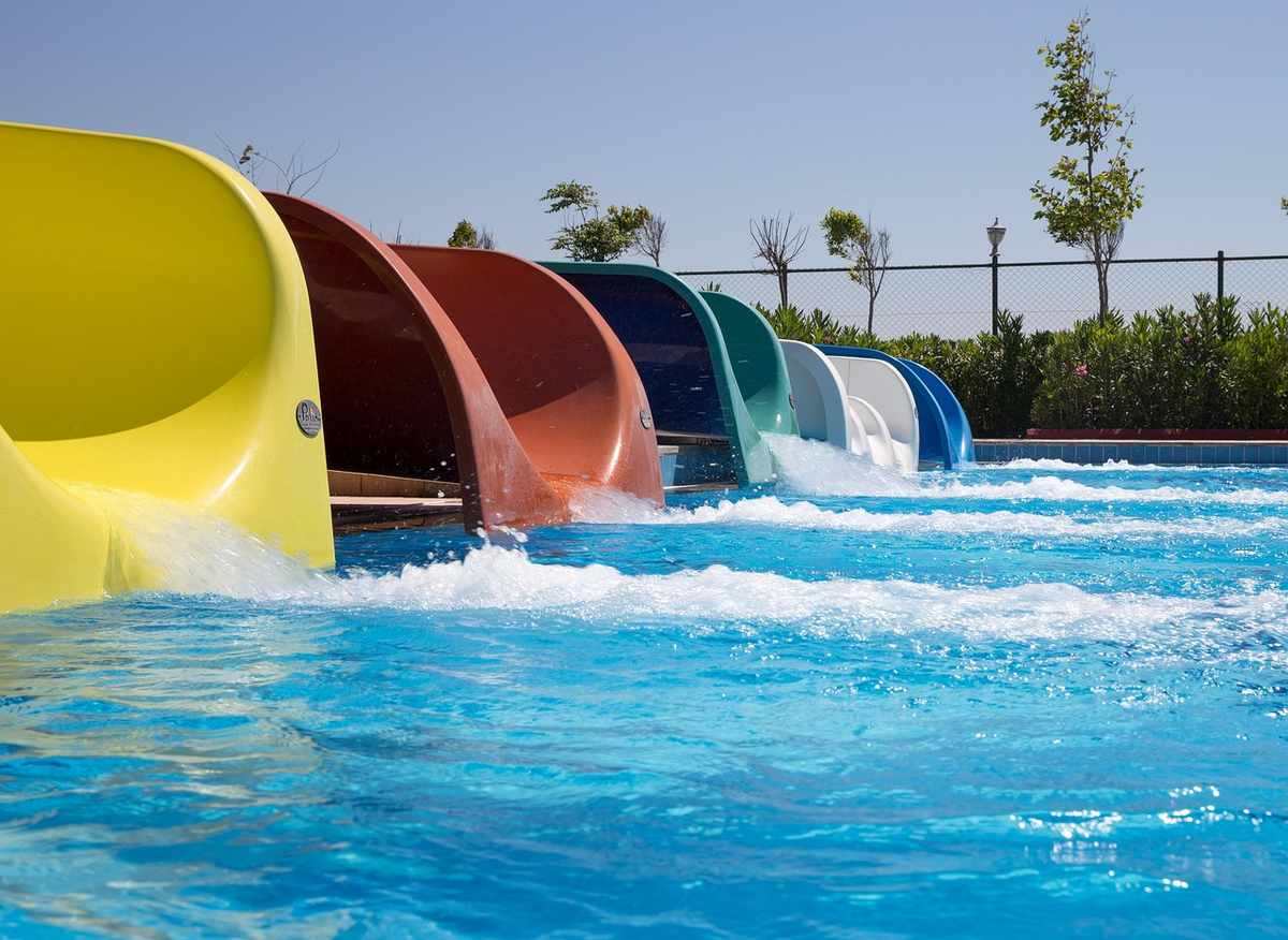 Glissades aquatiques colorées dans une piscine, avec végétation et clôture en arrière-plan