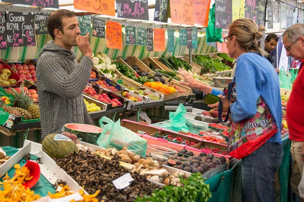 Un homme mange un fruit au stand de légumes une femme le regarde Un homme mange un fruit au stand de légumes une femme le regarde