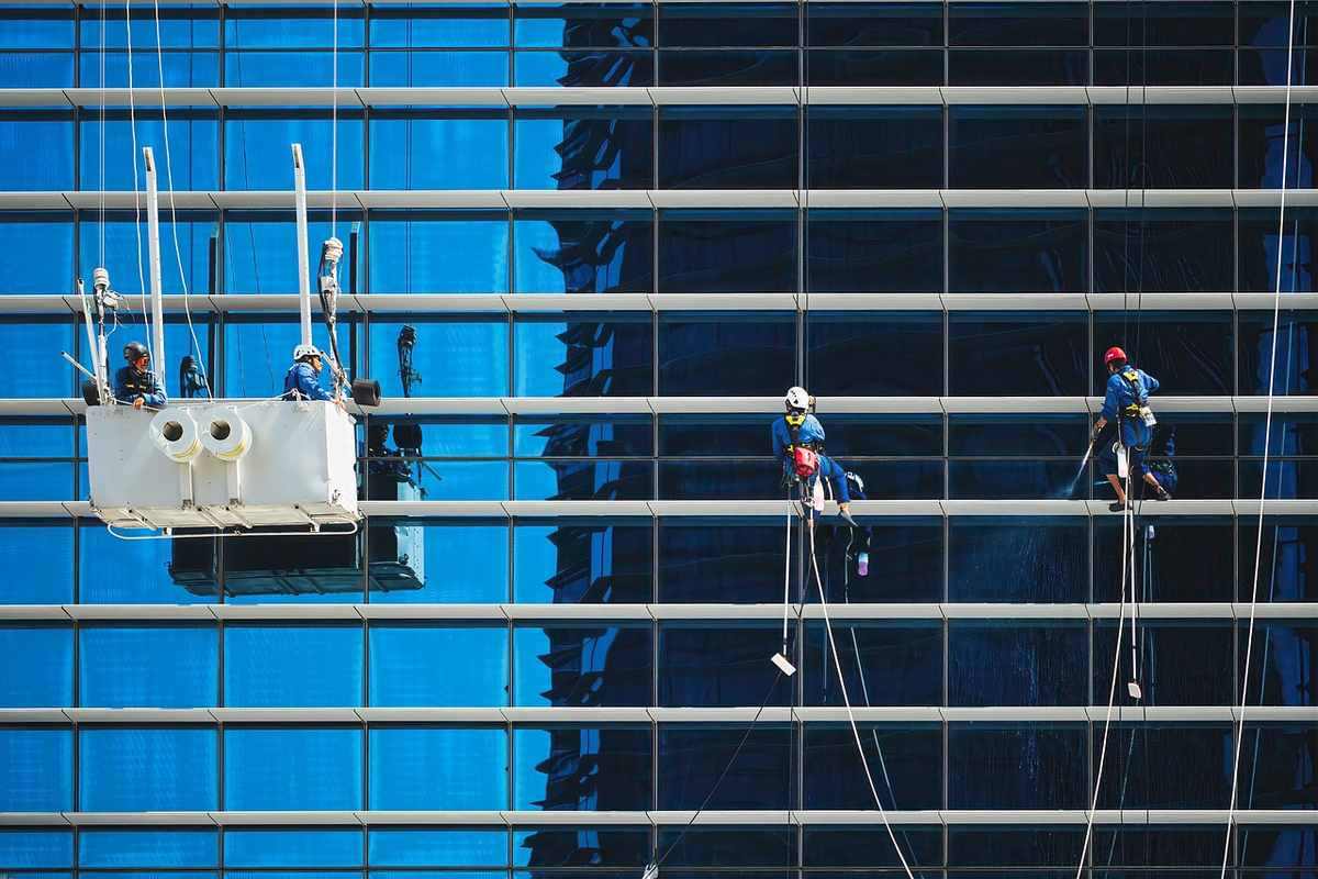 Travailleurs en harnais nettoient les vitres d'un gratte-ciel sous un ciel bleu