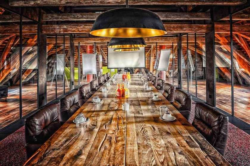 Grande table en bois, chaises en cuir, lumières suspendues, salle de réunion