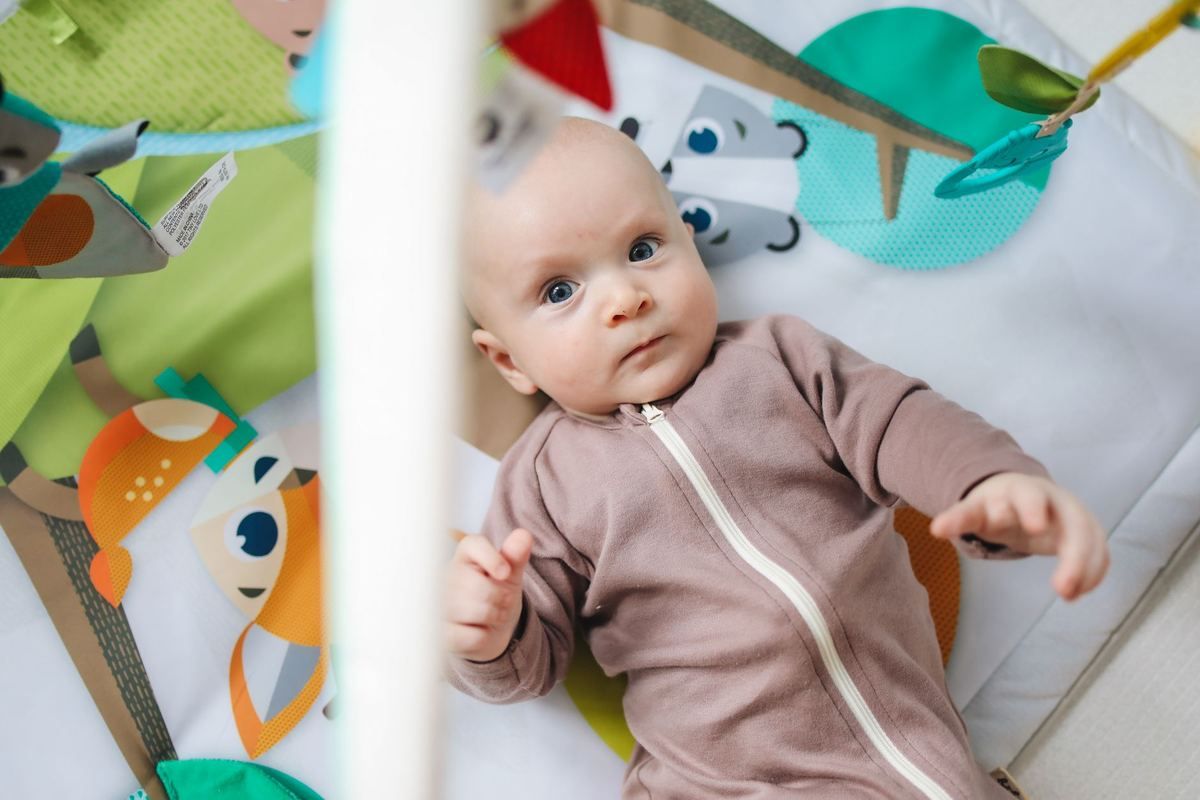 Nourrisson en body gris sur tapis d'éveil coloré avec jouets pédagogiques suspendus
