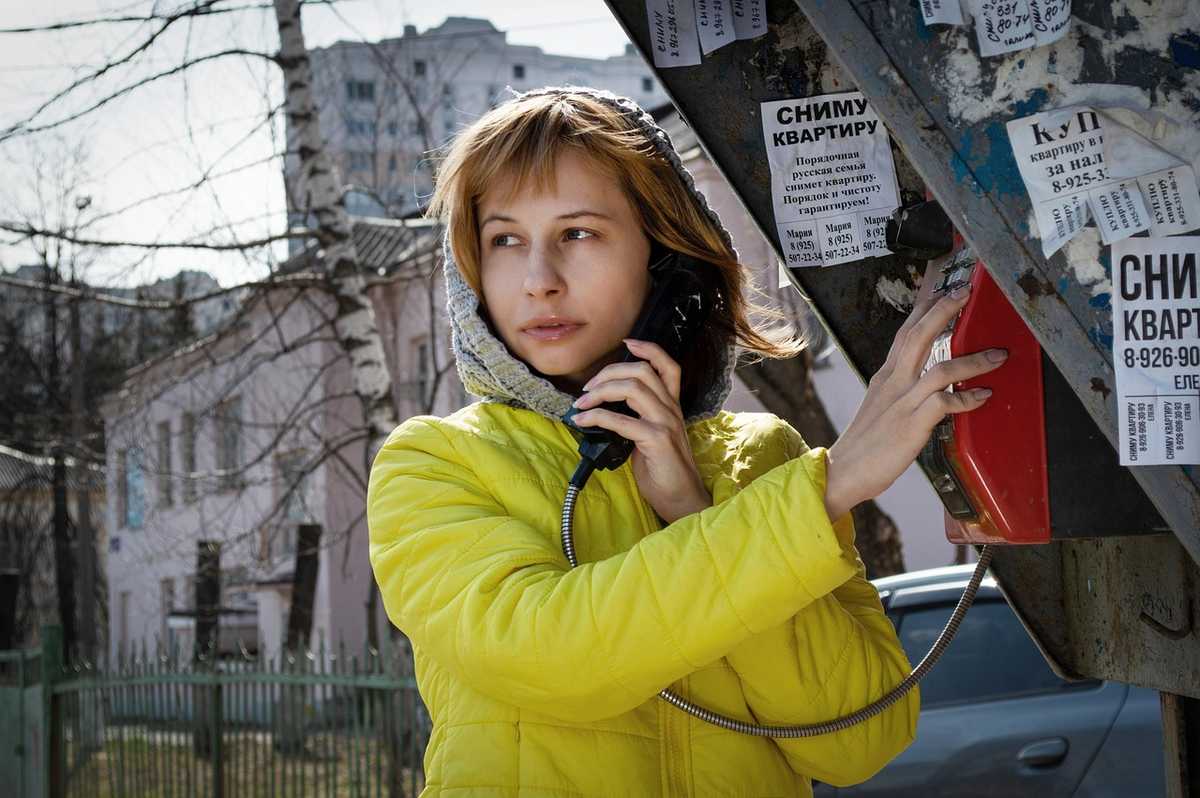 Une femme en veste jaune parle au téléphone rouge à l'extérieur