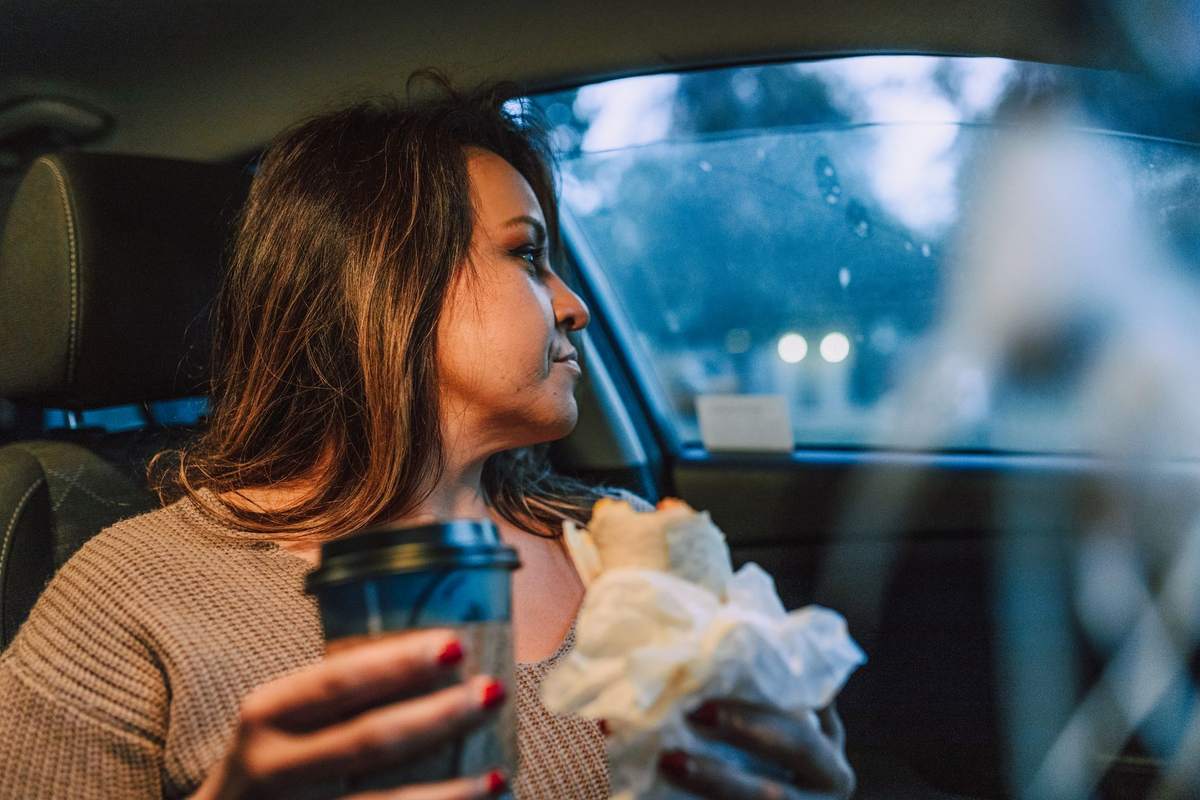 Une femme assise dans une voiture, tenant un café et un sandwich
