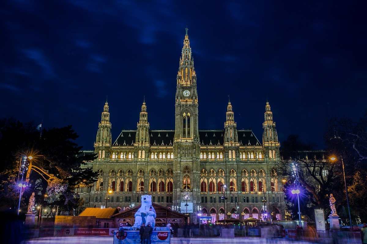 Bâtiment gothique majestueux illuminé de nuit, place devant avec statues et fontaine