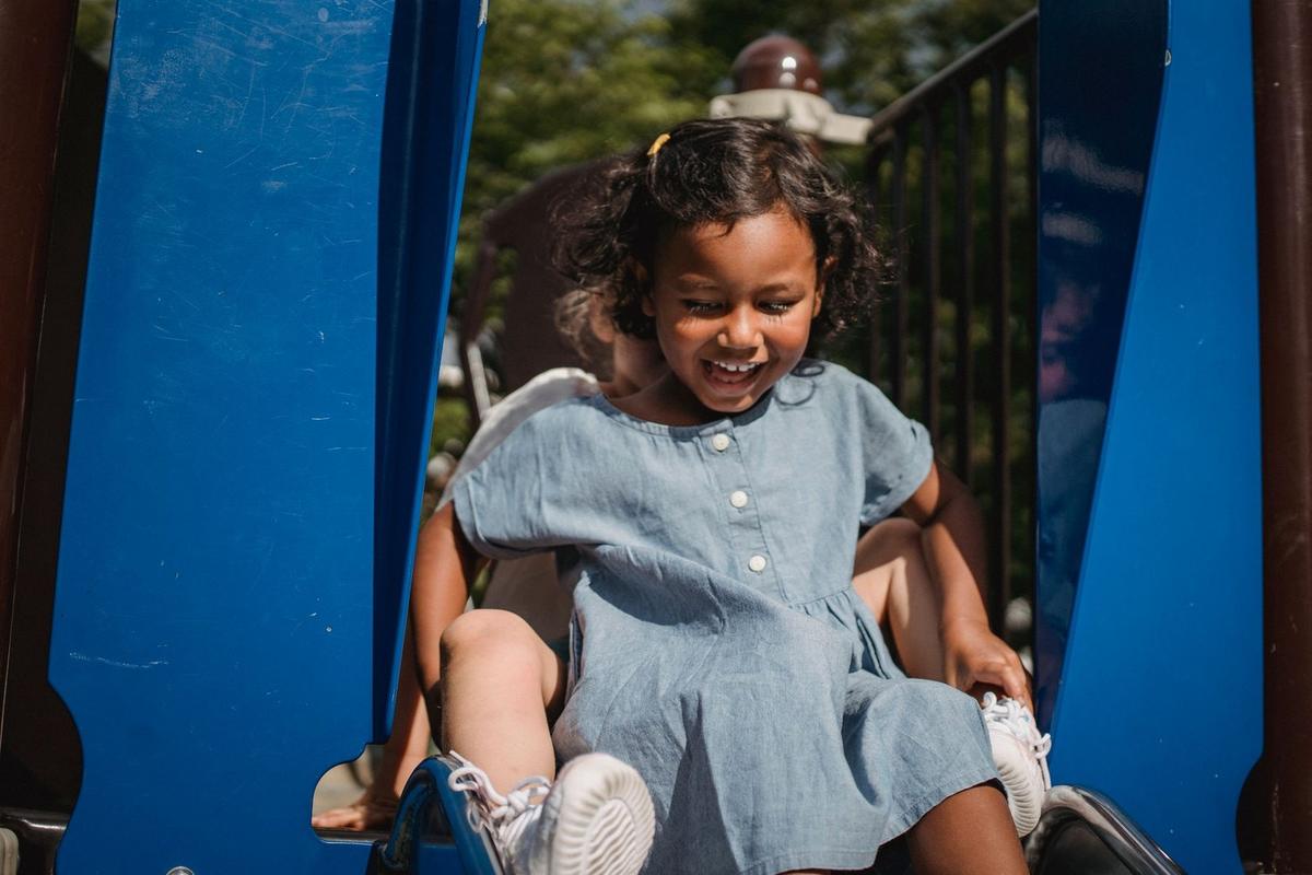 Enfant joyeuse sur une balançoire, vêtue d'une robe bleue, dans un parc ensoleillé Enfant joyeuse sur une balançoire, vêtue d'une robe bleue, dans un parc ensoleillé