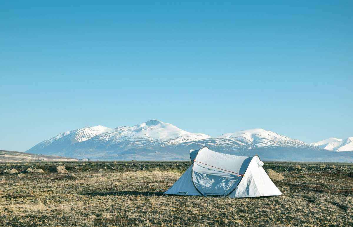 Tente blanche sur une prairie avec des montagnes enneigées en arrière-plan sous un ciel bleu Tente blanche sur une prairie avec des montagnes enneigées en arrière-plan sous un ciel bleu